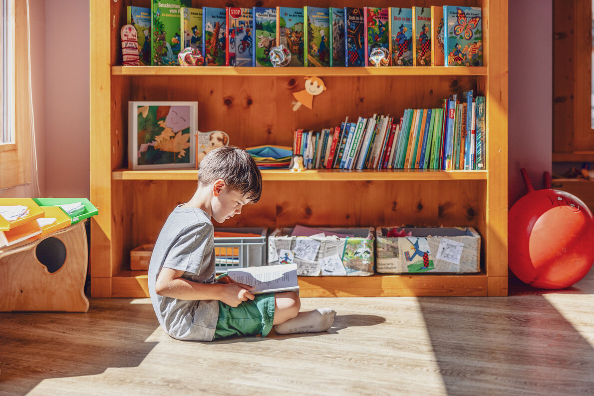 Ein Junge sitzt im Globi Kids Club im Hotel Waldhuus und schaut sich ein Globi Buch an.  | © DDO - davos.ch | Martin Bissig