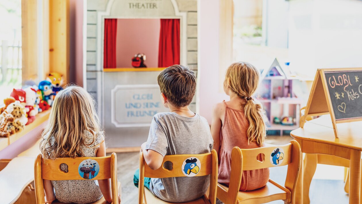 Drei Kinder sitzen vor dem Handpuppen Theater im Hotel Waldhuus und schauen sich ein Stück an. | © DDO - davos.ch | Martin Bissig