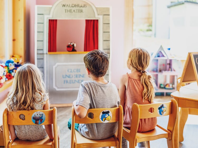 Drei Kinder sitzen vor dem Handpuppen Theater im Hotel Waldhuus und schauen sich ein Stück an. | © DDO - davos.ch | Martin Bissig