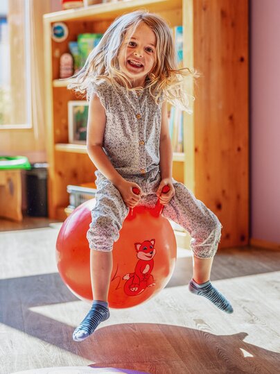 Ein Mädchen sitzt auf einem roten Ball und hüpft durch den Globi Kids Club im Hotel Waldhuus Davos. | © DDO - davos.ch | Martin Bissig
