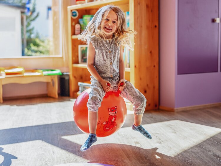 Ein Mädchen sitzt auf einem roten Ball und hüpft durch den Globi Kids Club im Hotel Waldhuus Davos. | © DDO - davos.ch | Martin Bissig