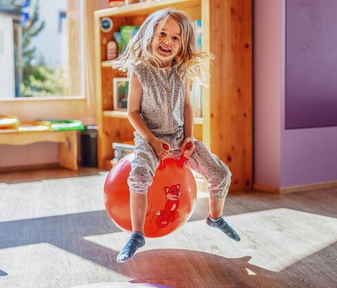 Ein Mädchen sitzt auf einem roten Ball und hüpft durch den Globi Kids Club im Hotel Waldhuus Davos. | © DDO - davos.ch | Martin Bissig