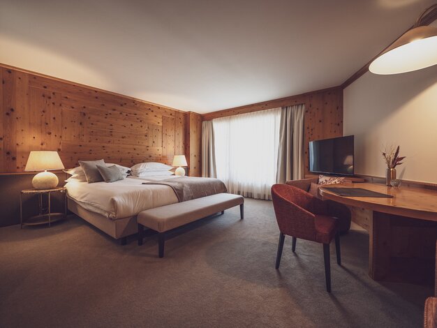 Grosses Hotelzimmer mit viel Holz, einem Doppelbett und einem Schreibtisch | © Davos Klosters Mountains