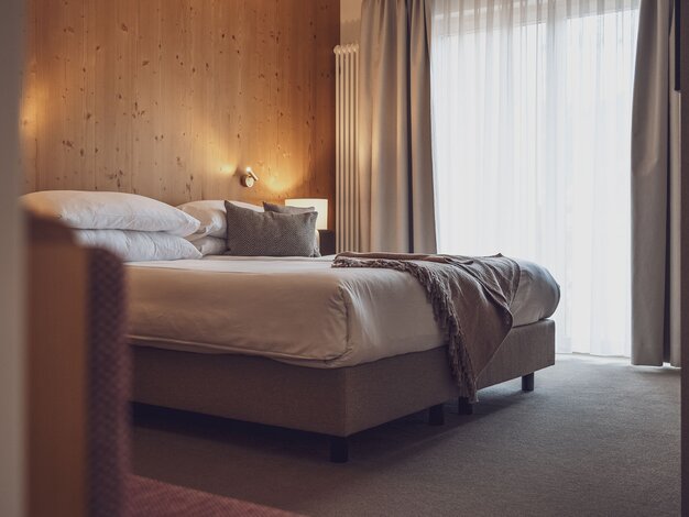 Doppelbett mit Bettwäsche und Vorhängen  | © Davos Klosters Mountains 