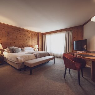 Large hotel room with lots of wood, a double bed and a desk | © Davos Klosters Mountains